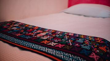 Una tela bordada y colorida sobre una cama con un almohadón blanco.