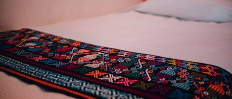 A colorful embroidered fabric laid on a bed with a white pillow.