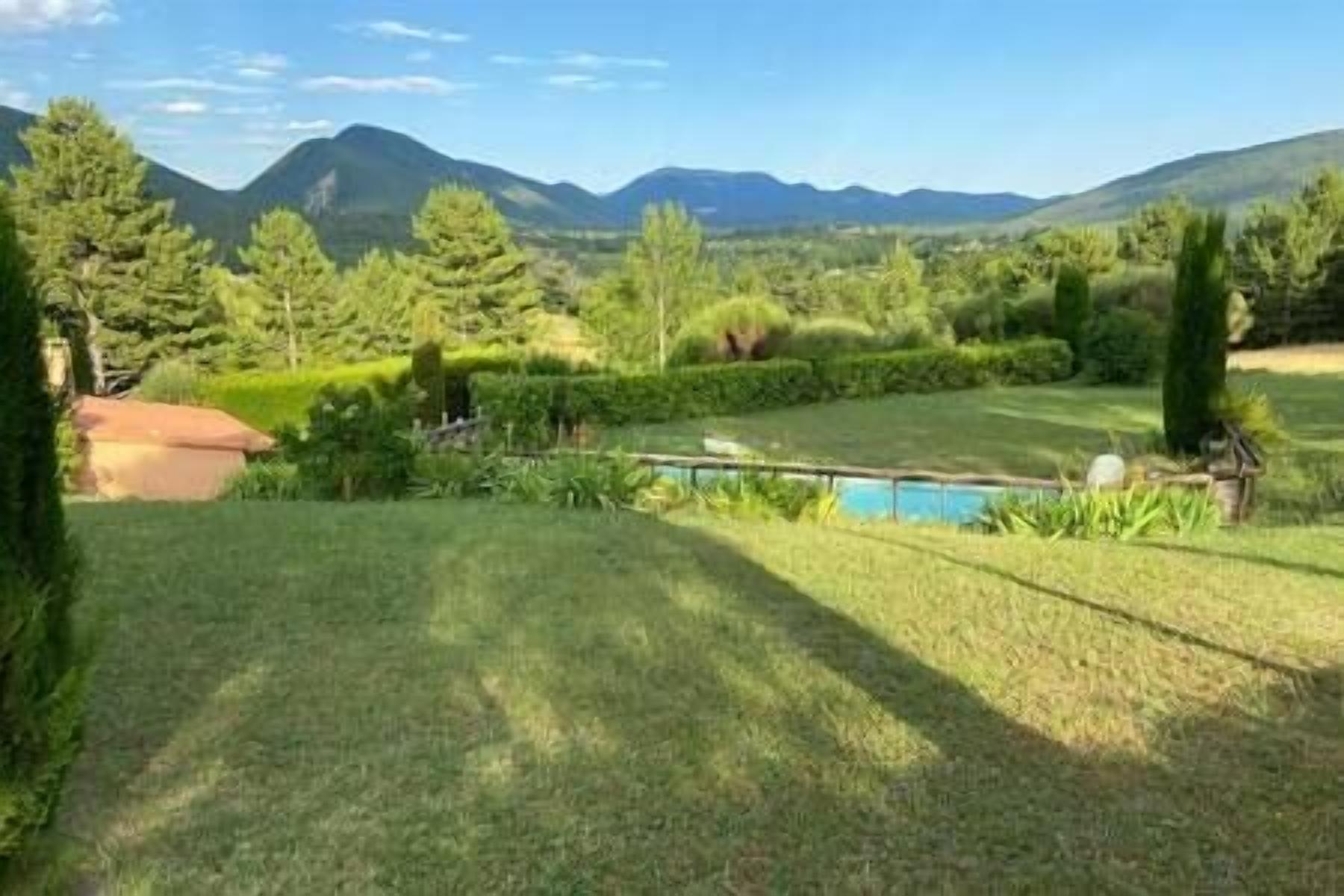 A grassy outdoor area with a swimming pool, surrounded by trees and mountains in the background.