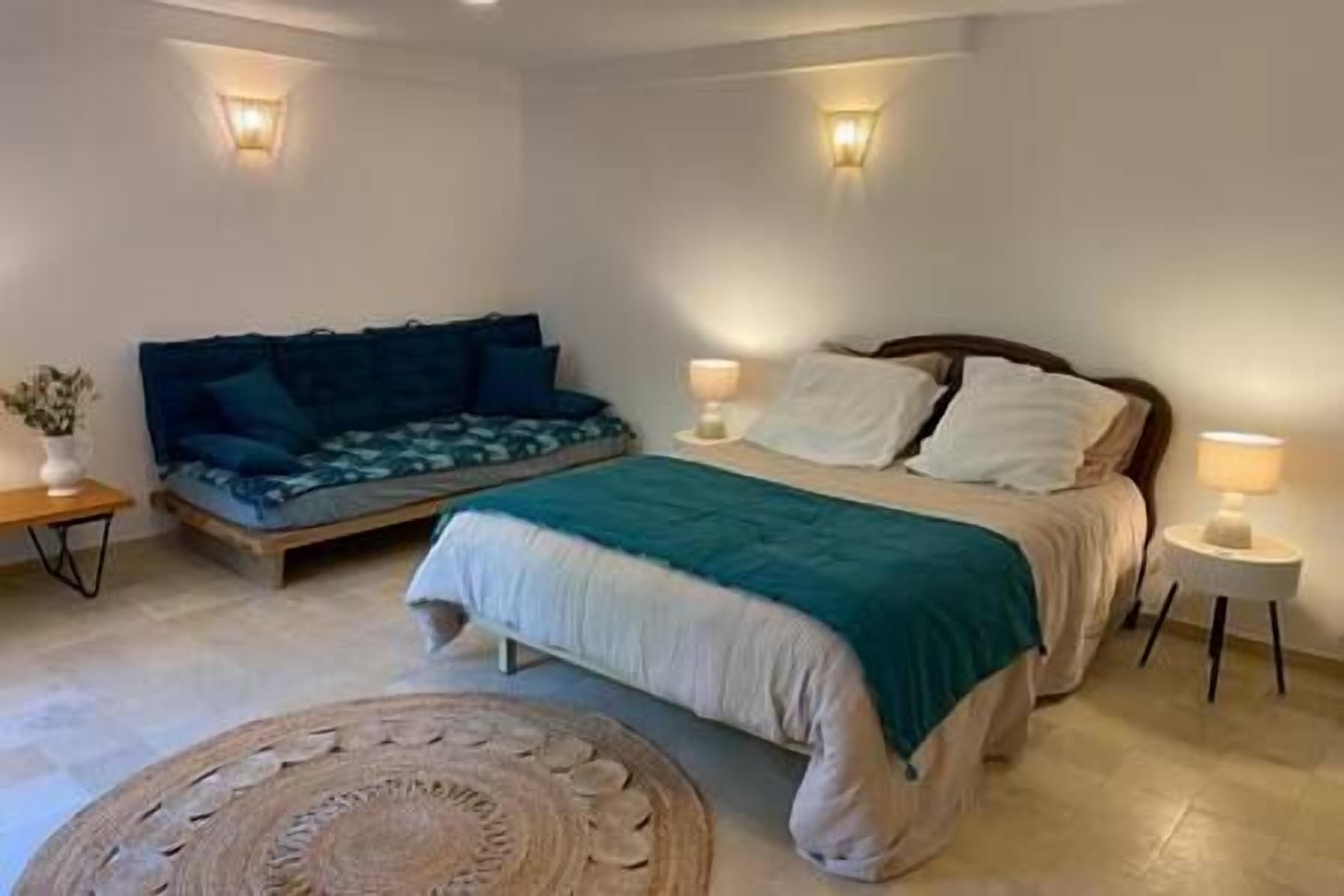 A bedroom with a bed, a sofa, two bedside tables, and a floor lamp.