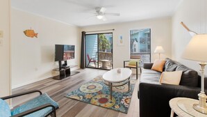 Un salon avec un canapé, une table basse, un téléviseur et un balcon offrant une vue agréable.