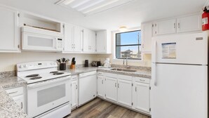 Une cuisine moderne avec des meubles blancs, un four à micro-ondes encastré, une cuisinière et un réfrigérateur.