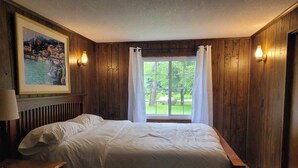 A bedroom with a large bed, a bedside table, a framed painting, and a window with curtains. - Lake Front on Little Clear Lake- Comfort Resort (Prescott)