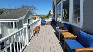 Eine Holzterrasse mit Gartenmöbeln, darunter eine Sitzecke mit Sofa und Stühlen, sowie ein weißes Geländer.