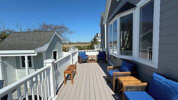 Une terrasse en bois, aménagée avec du mobilier d’extérieur, notamment un canapé et des fauteuils, et dotée d’une rambarde blanche.