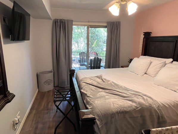 A bedroom with a bed, a desk, a chair, a TV, and a window with curtains.