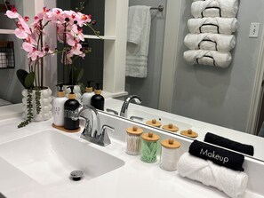 Un baño con lavamanos blanco, un espejo y un perchero con toallas dobladas con cuidado.