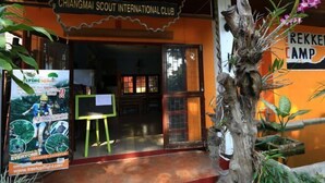 L'entrée du Chiangmai Scout International Club est agrémentée d'une sculpture en bois représentant un arbre et d'une affiche faisant la promotion d'expériences de vol dans les arbres.