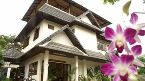 Une maison à deux étages, avec un toit recouvert de tuiles, une véranda ornée de plantes en pot et un vélo garé à l’extérieur.