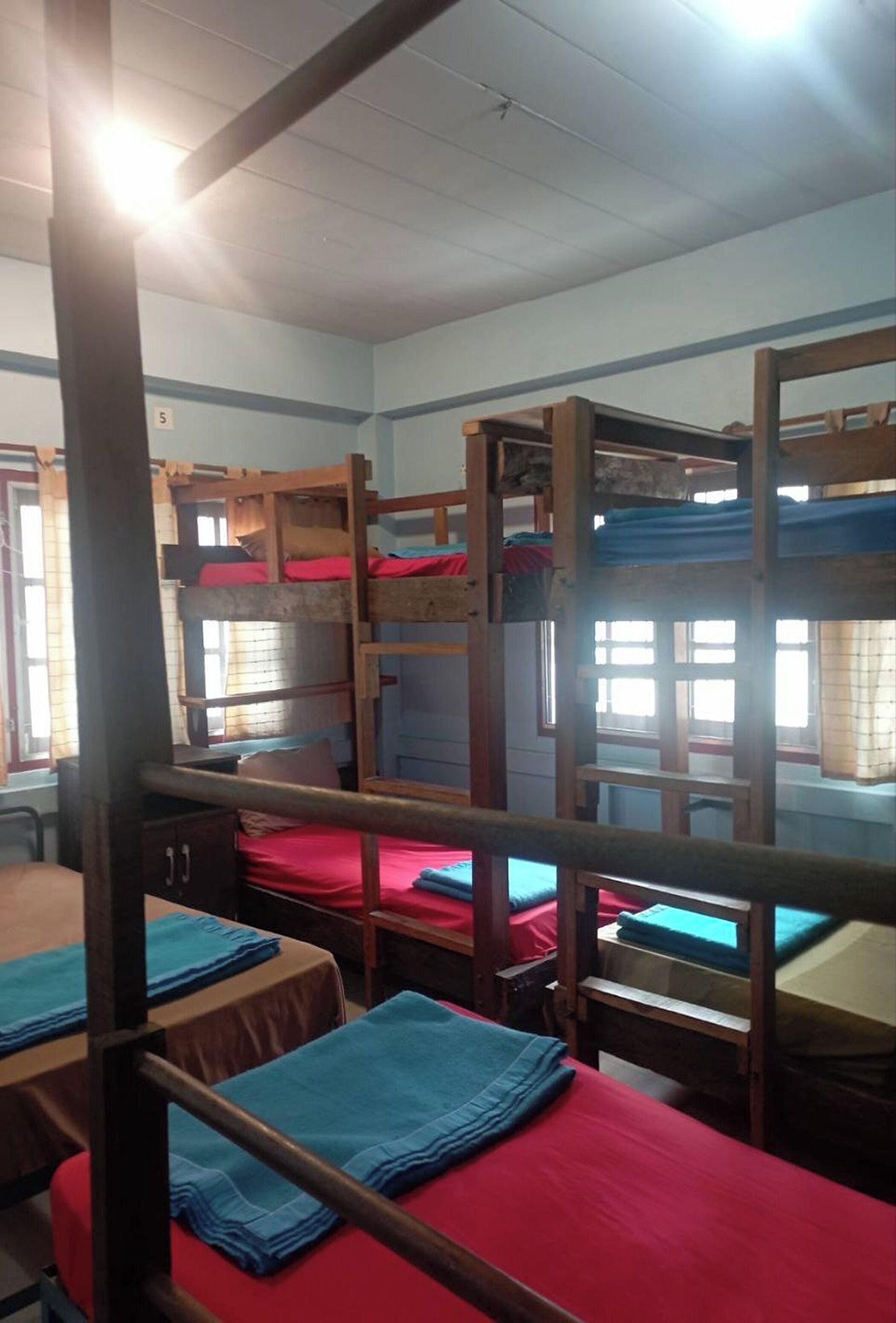 Une chambre de dortoir avec des lits superposés, des bureaux en bois et des draps rouges.