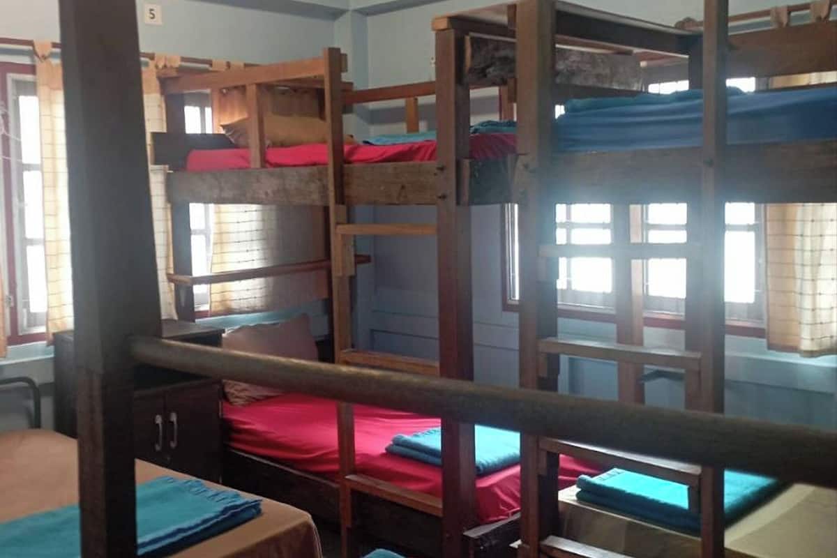 Een slaapzaal met stapelbedden, houten bureaus en rode lakens.