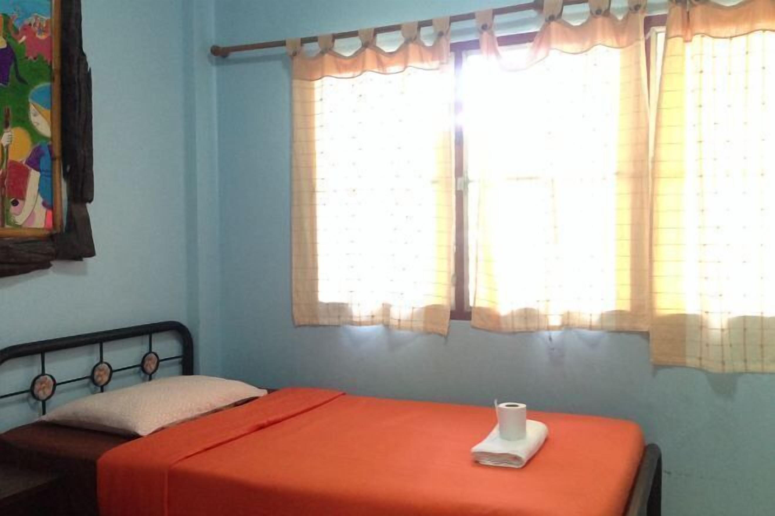 A room with a bed, a window with curtains, and a wall with a colorful painting.