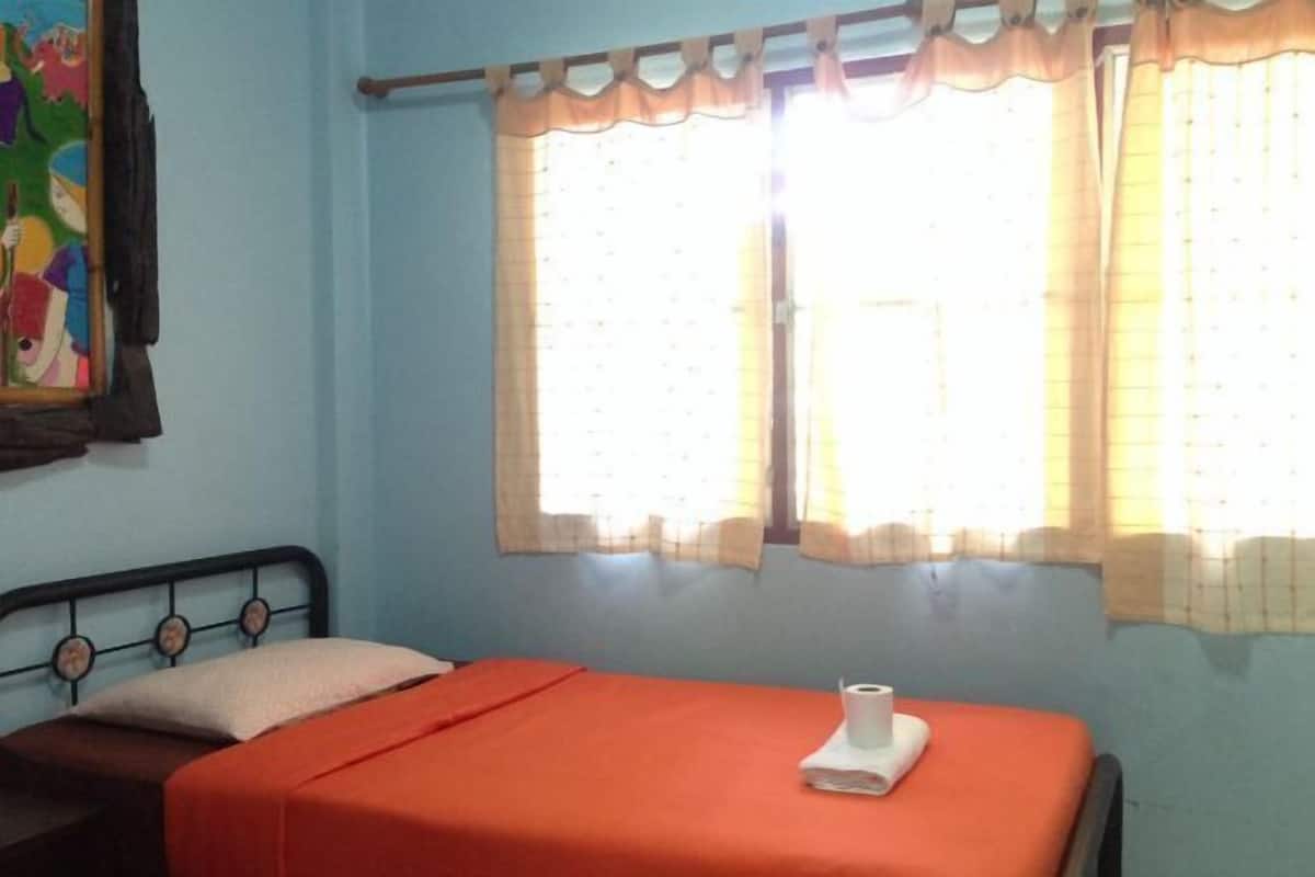 Een kamer met een bed, een raam met gordijnen en een muur met een kleurrijk schilderij.