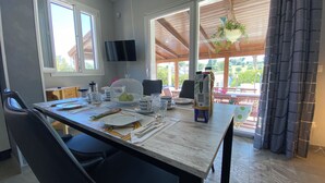 A dining area with a table set for two, a television on the wall, and a view of the outdoors. - 2 Bedroom Villa in Gallina (Gallina)