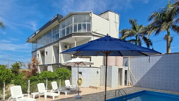 A modern two-story building with a swimming pool, stone flooring, and white lounge chairs. - Pousada Mar Alto (Ilha Comprida)
