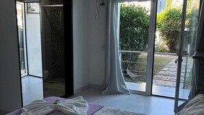 A bedroom with a bed, a TV, a sliding glass door to a balcony, and a shower area. - Pousada Mar Alto (Ilha Comprida)