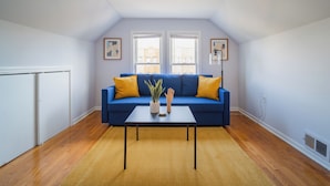 A living room with a blue sofa, a small table with a plant and a hand sculpture, and two windows with city views. - 2F - ❤️ Lowest Rates! Fun & Stylish 3BR in Logan Square (Chicago)