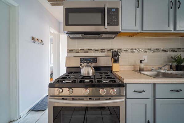 Una cocina con estufa de acero inoxidable, microondas y pileta.