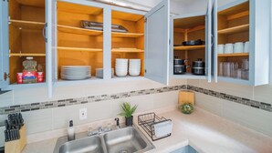 A kitchen with open cabinets displaying dishes, cookware, and a plant. - 2F - ❤️ Lowest Rates! Fun & Stylish 3BR in Logan Square (Chicago)