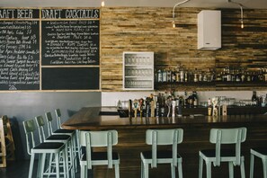 Un espace bar avec un mur en bois, un tableau noir affichant le menu des bières à la pression et des cocktails, et un comptoir bien garni de bouteilles et de verres.