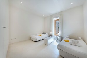 A modern hotel room with two beds, a bench, a small table, and a window with curtains. - Casa con Piscina en Selva (Selva)