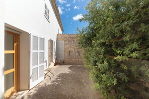 A courtyard with a stone wall, a white building with shutters, and a tree. - Casa con Piscina en Selva (Selva)