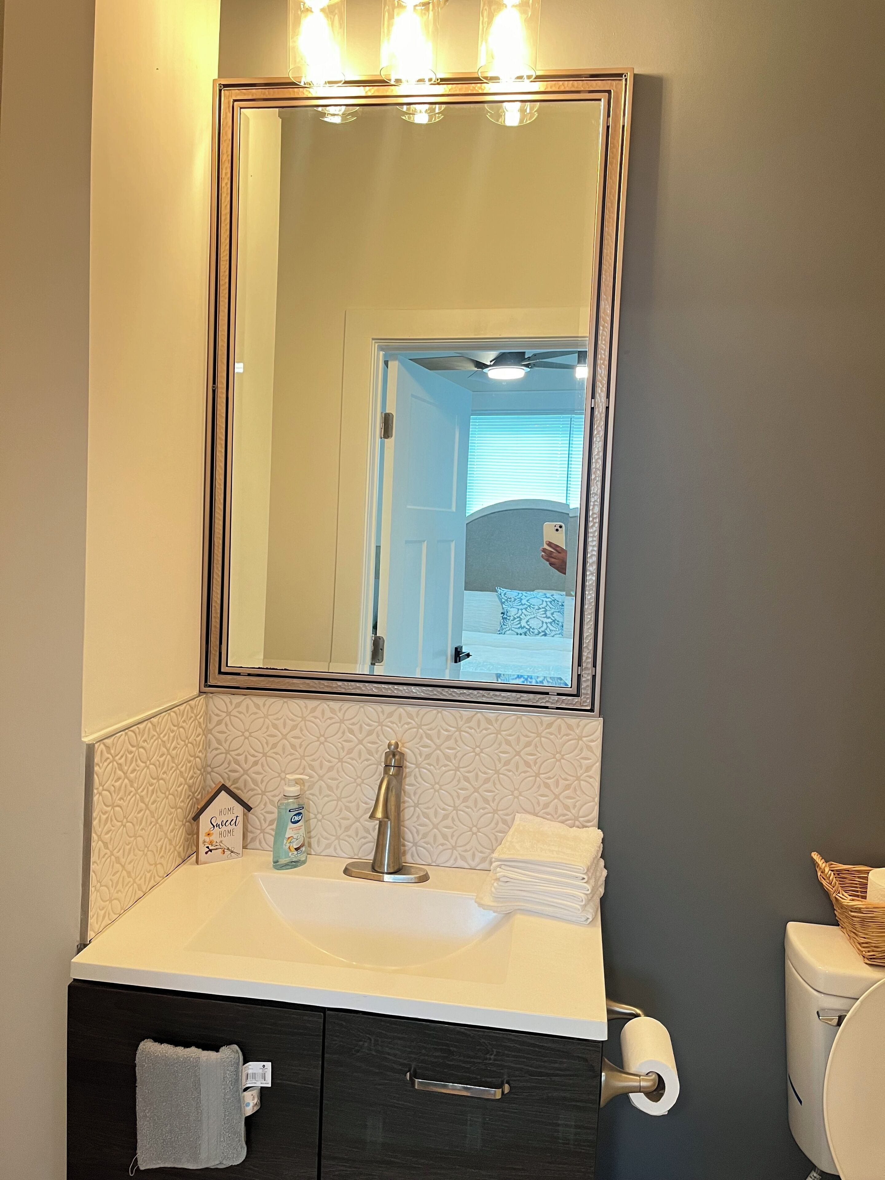 Um banheiro com uma pia branca, um espelho acima, porta-toalhas, vaso sanitário e parede com textura.