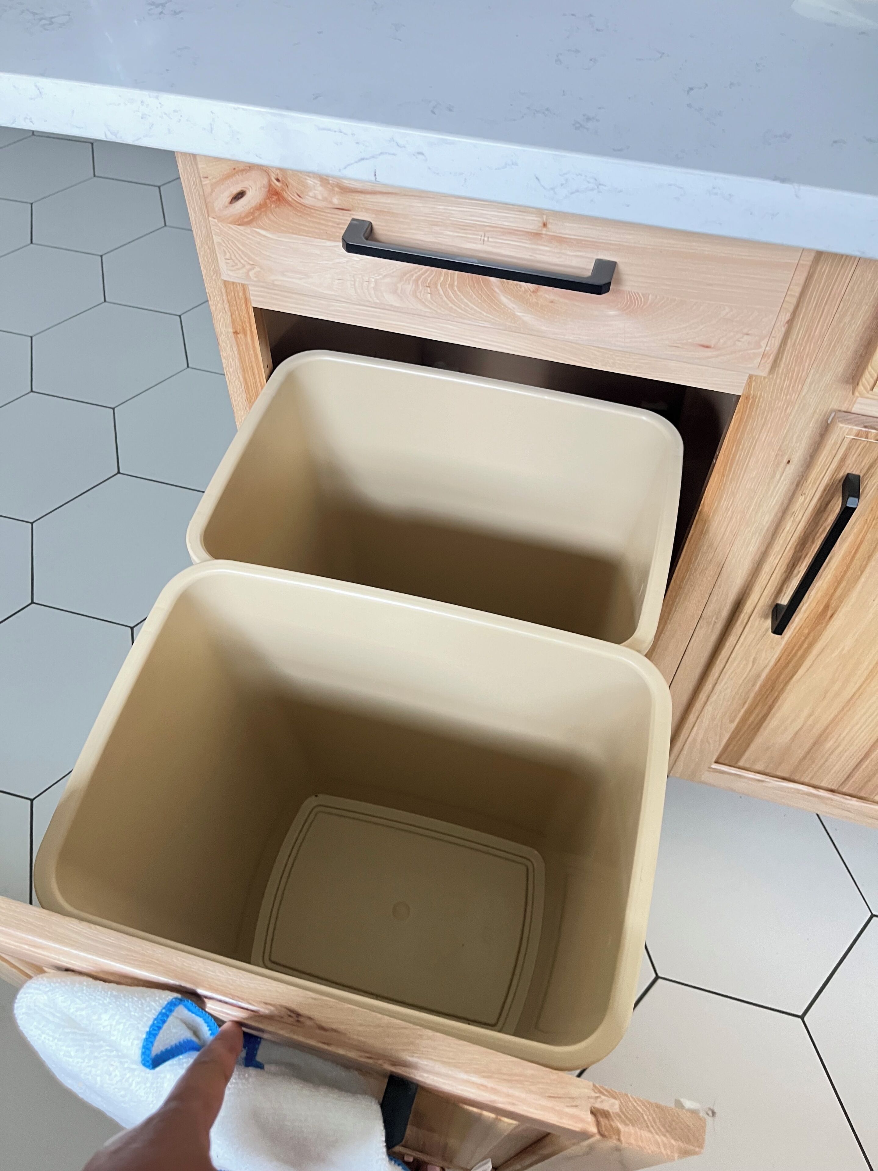 A kitchen with two beige storage bins under a wooden cabinet with a black handle.