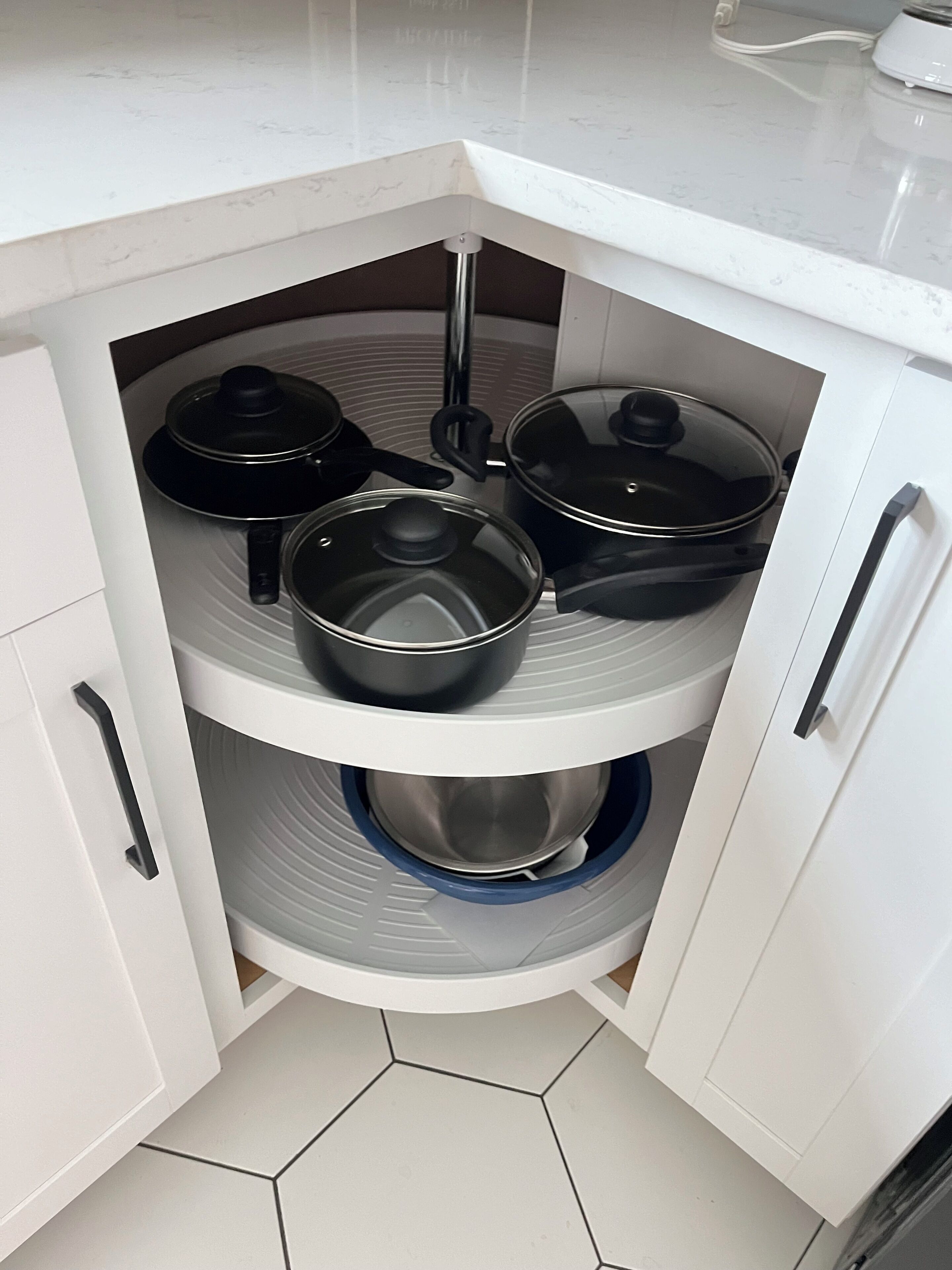 A kitchen with white cabinets and a built-in stove. There are three pots and pans on the stove, and a blue dish rack below.