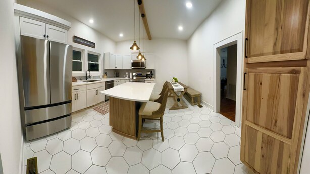 Une cuisine moderne dotée d’un réfrigérateur en acier inoxydable, de meubles blancs, d’une table à manger en bois et d’un revêtement de sol en carrelage hexagonal.