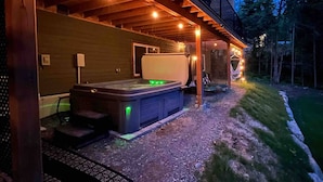 Ein Whirlpool mit Stufen und überdachtem Bereich, umgeben von einer Holzterrasse und Außenbeleuchtung.