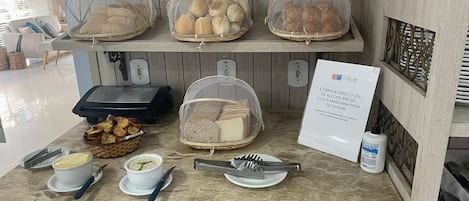 A breakfast buffet setup with bread, pastries, and condiments.