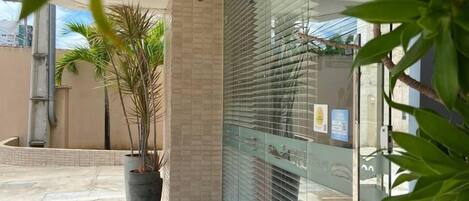 Un edificio moderno con fachada de vidrio, plantas en macetas y un patio con baldosas.