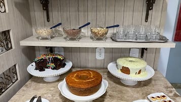 Una encimera de cocina con varios productos de repostería, incluyendo un pastel de chocolate con confeti, un pastel simple y un pastel tipo rosca con glaseado. También hay platos con galletas y una bandeja de vasos.