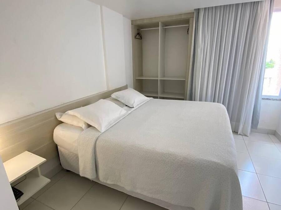 Una habitación de hotel con una cama grande, un vestidor y una ventana con cortinas.