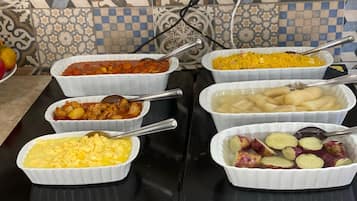 Une table de buffet proposant divers plats présentés dans des bols blancs, notamment un ragoût de légumes, un plat de riz jaune, des œufs brouillés et des pommes de terre en tranches.