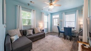 A living room with a grey sofa, blue chairs, a ceiling fan, and a TV.