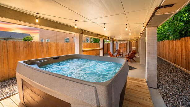 A hot tub with a wooden deck, a covered patio area, and a view of a house in the background.