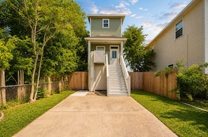 A two-story house with a front yard, a wooden fence, and a staircase leading to the front door.