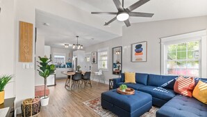 A modern living room with a sectional sofa, a dining area with a table and chairs, and a kitchen in the background. - Historic Cottage Walk to Downtown St Augustine Free Parking Sleeps 4 (St. Augustine)