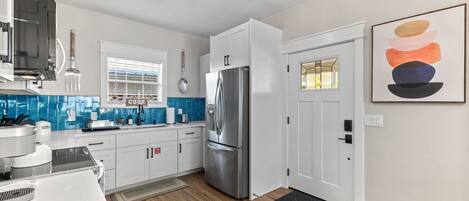 A modern kitchen with white cabinets, a stainless steel refrigerator, and a blue-tiled backsplash.