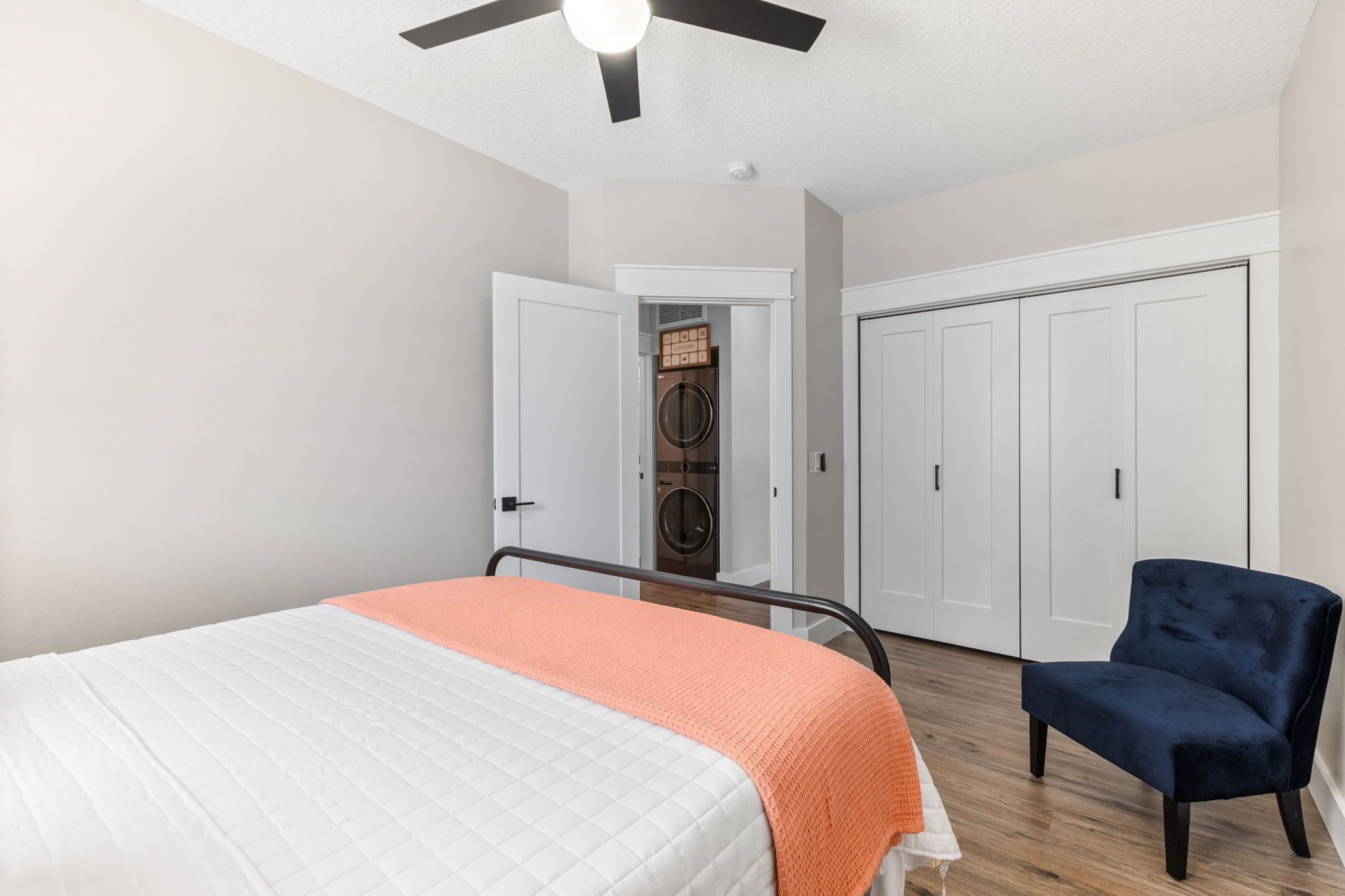 Un dormitorio con cama, una silla, ventilador de techo y vestidor.
