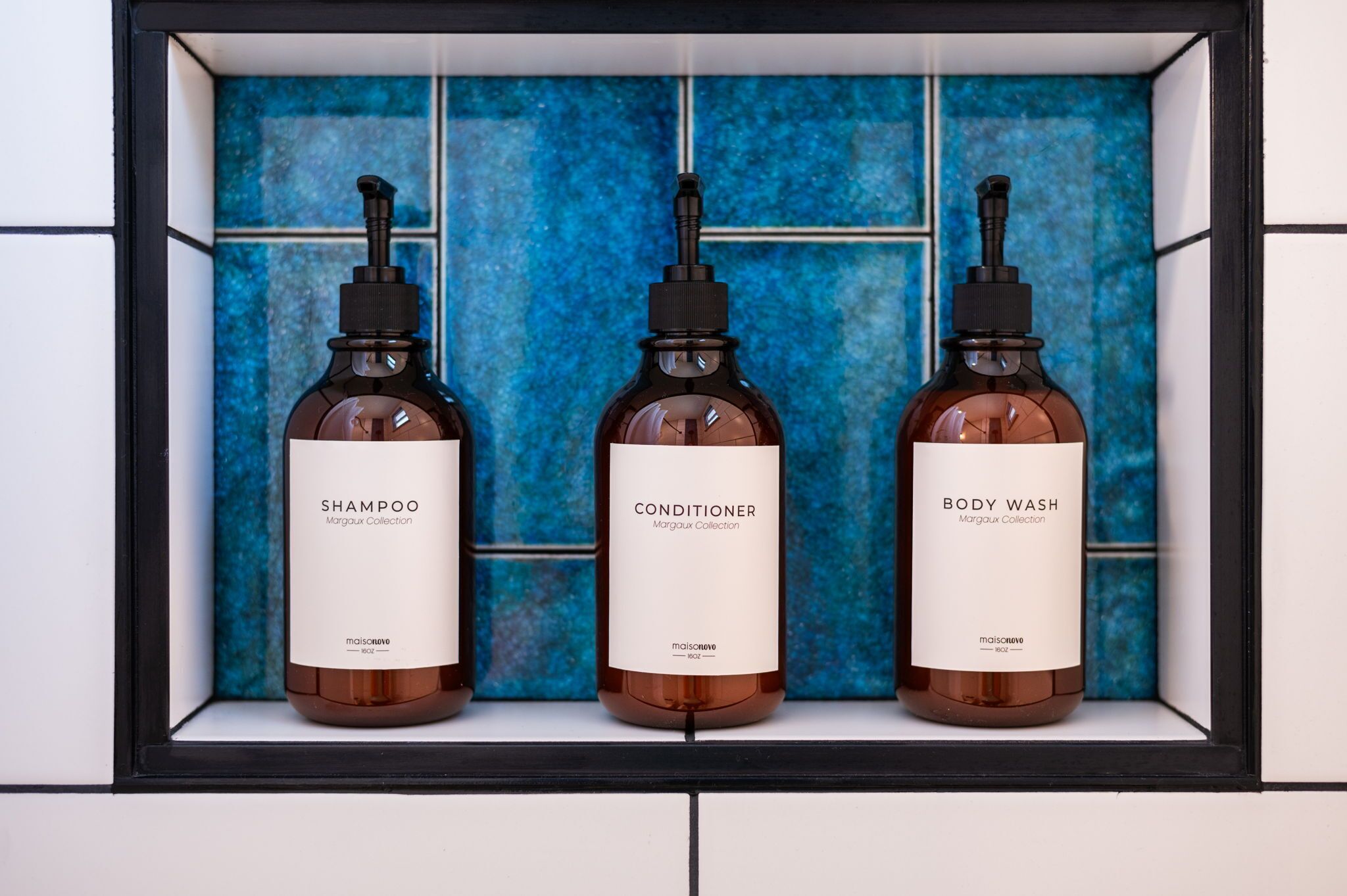 Three bottles of skincare products in a black-framed display against a blue-tiled wall.
