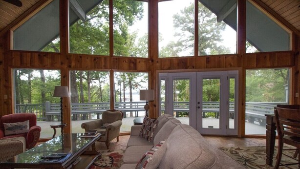 Amplia sala de estar con un sofá grande, una mesa de centro y una chimenea. Amplias ventanas ofrecen vistas al exterior.