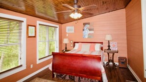 Un dormitorio con techo de madera, una cama, dos mesitas de noche con lámparas y una ventana con persianas.