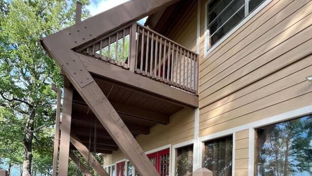 Una terraza de madera con una escalera que sube a un balcón en un segundo piso.