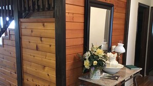 Una pared de madera con un espejo, un jarrón con flores, un cuenco y una lámpara sobre una mesa.