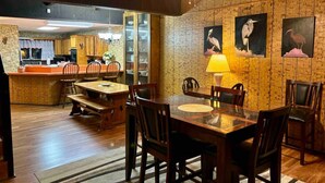 Un comedor con mesa y sillas de madera, un ventilador de techo y obras de arte colgadas en la pared.