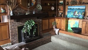 Una sala acogedora con chimenea de ladrillo, estanterías de madera y un cuadro grande.