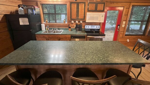 A kitchen with granite countertops, wooden cabinets, a black refrigerator, a stove, and a microwave. - Leisure Lake Cabin, Toledo Bend Lake (Many)